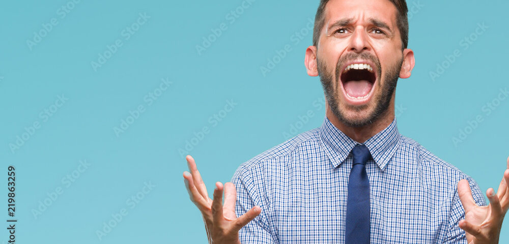 Young handsome business man over isolated background crazy and mad shouting and yelling with aggressive expression and arms raised. Frustration concept.